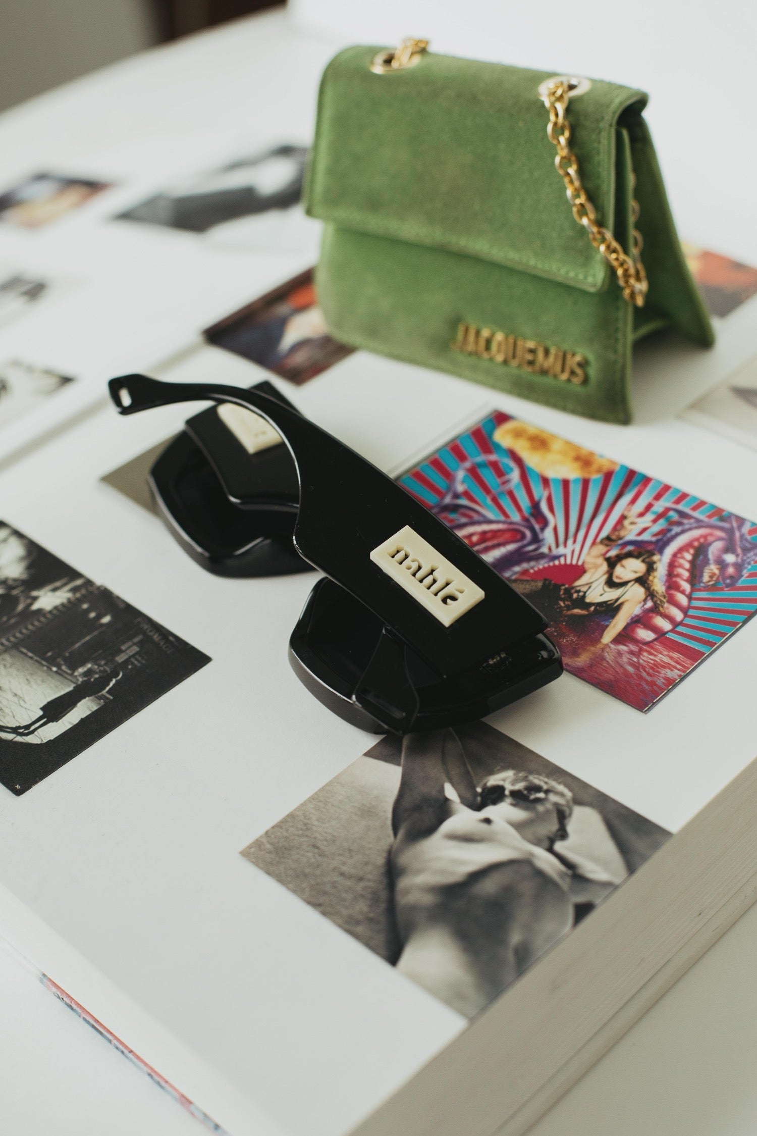 Green handbag with gold chain, black sunglasses, and vintage photos on a white surface