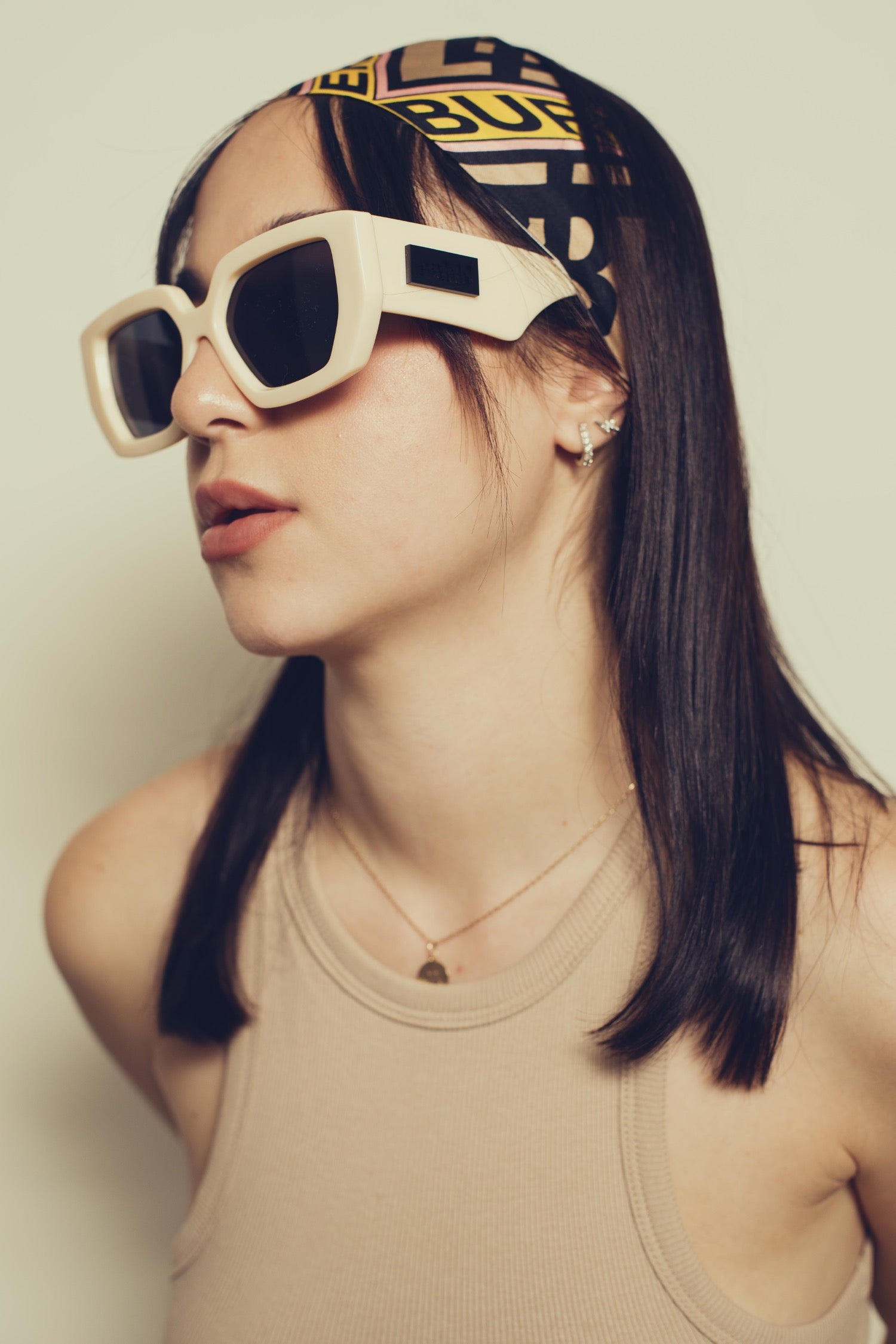 Person wearing large sunglasses and a patterned headband against a plain background