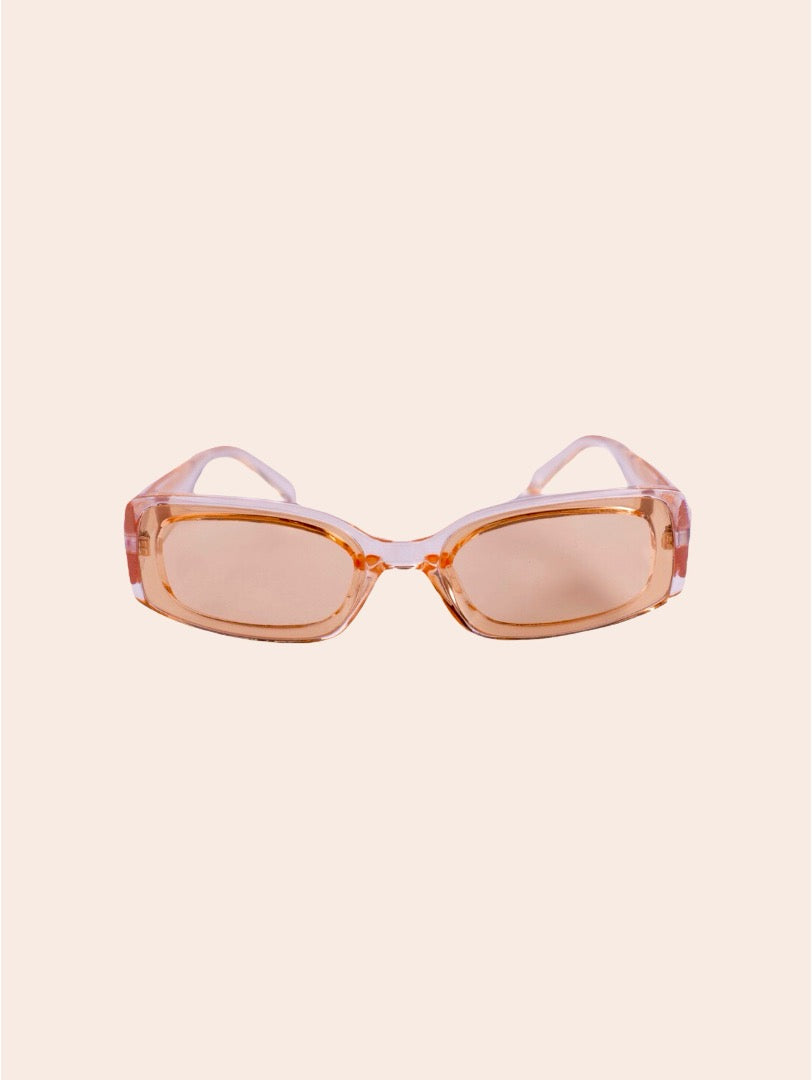 A pair of oversized square sunglasses with translucent peach-orange frames and light pink lenses, shown against a solid pale beige background.