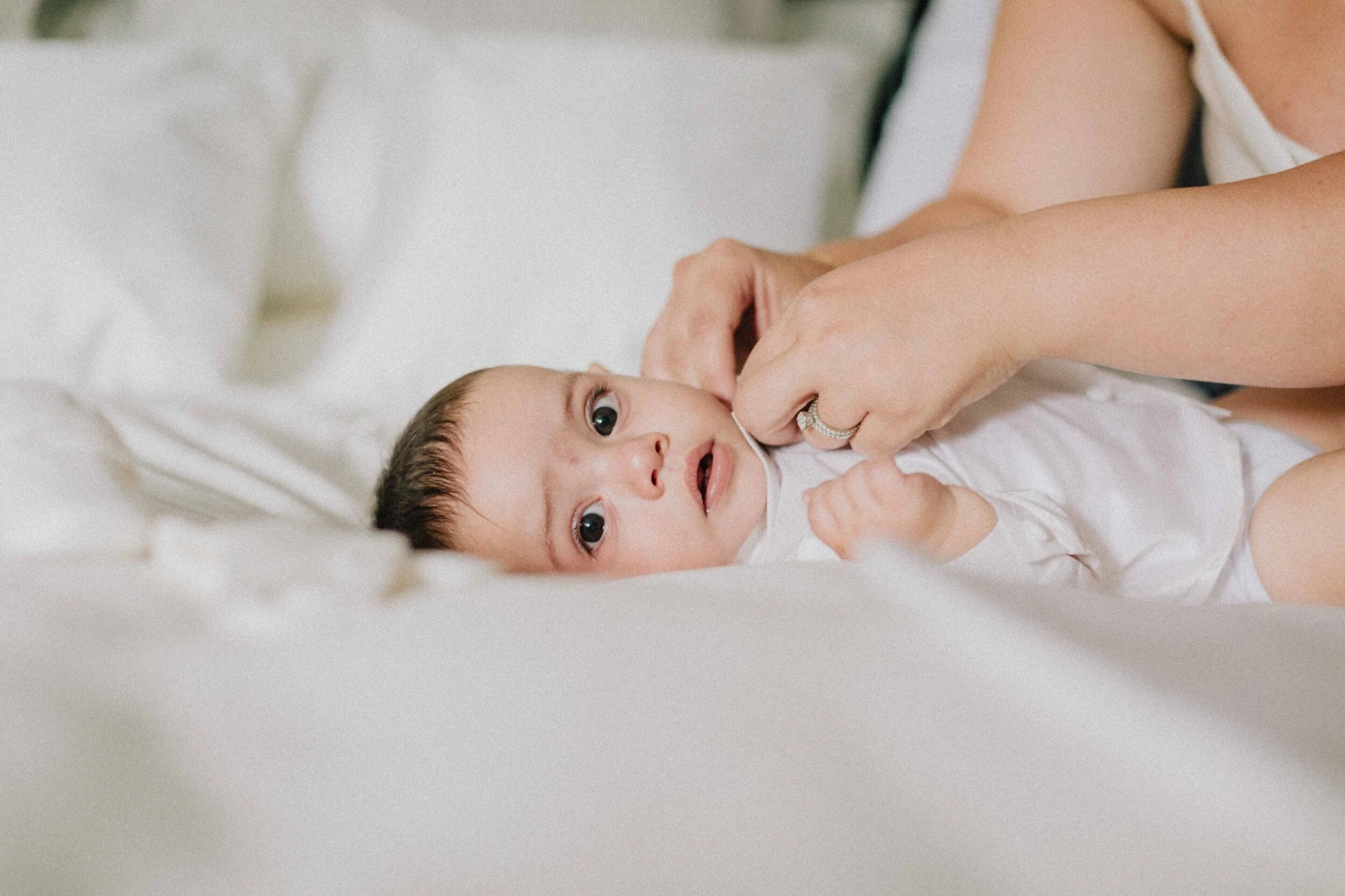 Baby lying on a white blanket with a person's hand near